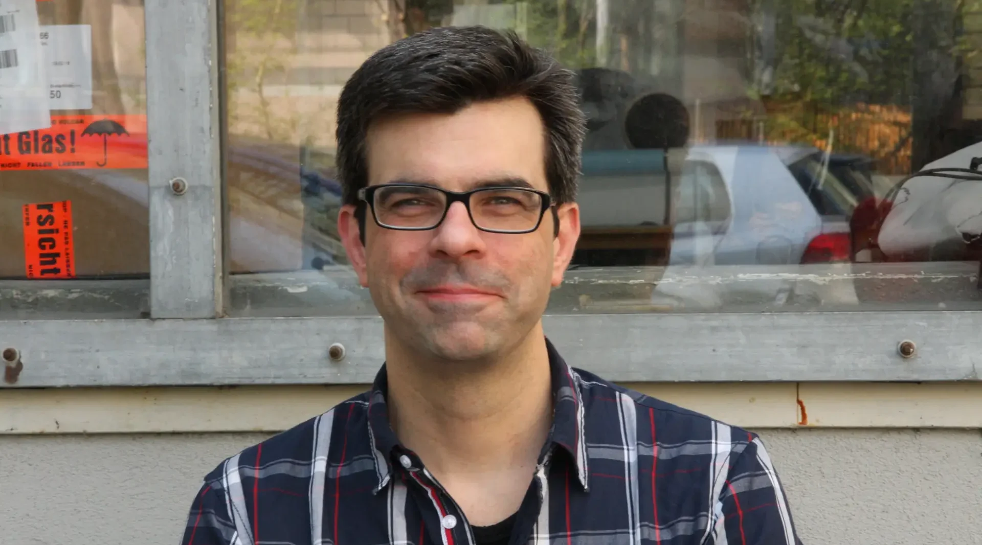 Portrait Andre Witting, Modellbauer bei werk. Ein Mann mit kurzen dunklen Haaren, kariertem Hemd und dunkler Brille.